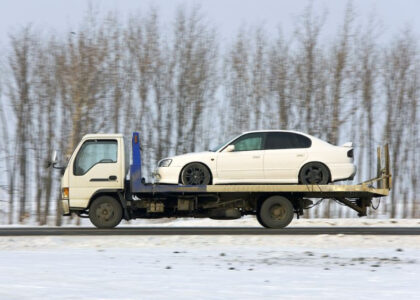 White sedan being towed on a flatbed truck, emphasizing commercial vehicle transport in snowy conditions, relevant to commercial auto insurance cost discussions.