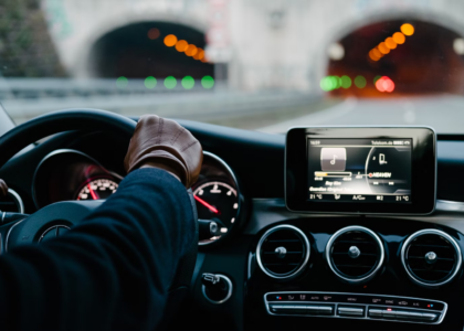 Driver's hand on steering wheel of a luxury car approaching a tunnel, featuring a dashboard display with music controls, illustrating high-risk driving scenarios relevant to Oregon SR-22 insurance.