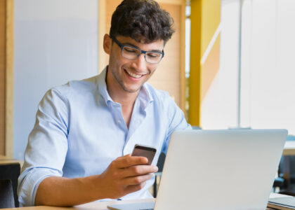 Young man using laptop and cell phone to learn how to reinstate his driver's license.