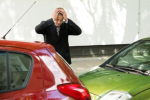 A man who will need Florida non-owner SR22 or FR44 insurance, standing in front of his damaged car after an accident.