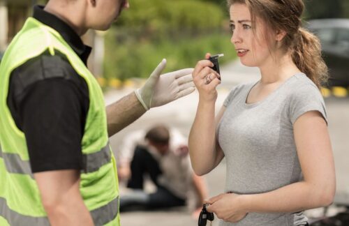 A young woman is taking a breathalyzer test after a car accident.