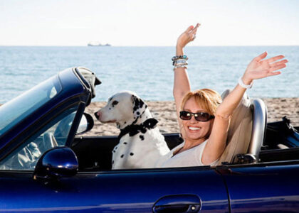 Woman in convertible car with dog, enjoying a beach day, representing freedom and leisure, relevant to discussions on non-owner and high-risk auto insurance.