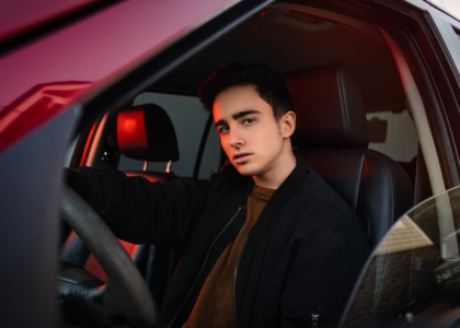 Teenage driver sitting in a car, looking confidently at the camera, emphasizing the importance of responsible driving and insurance in high-risk scenarios.
