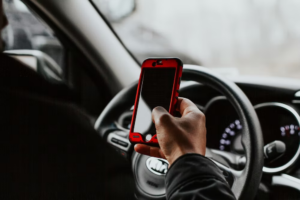 A man holding a cell phone while driving his car.