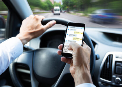 Driver holding a smartphone while steering through fast highway traffic, illustrating distracted driving in the context of Missouri's hands-free driving law.