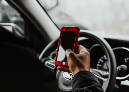 A man holding a cell phone while driving his car.