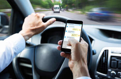 Driver holding a smartphone while steering through fast highway traffic, illustrating distracted driving in the context of Missouri's hands-free driving law.