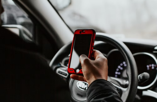 A man holding a cell phone while driving his car.