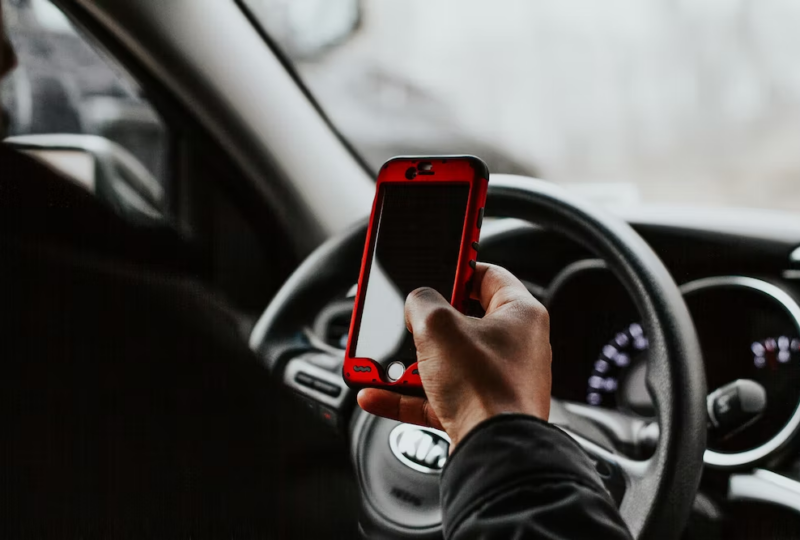 A man holding a cell phone while driving his car.