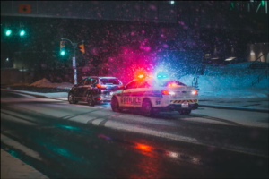 Police car with lights flashing pulls a car over to the side of a snowy Missouri road.