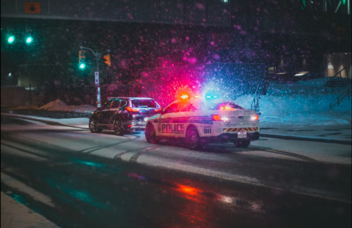 Police car with lights flashing pulls a car over to the side of a snowy Missouri road.