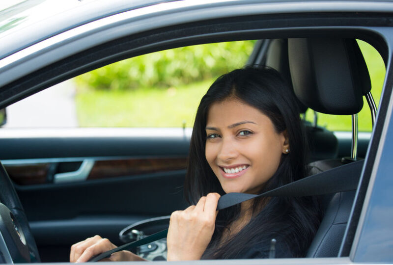 Smiling woman fastening her seatbelt in a car, representing safe driving practices related to Oregon SR-22 insurance requirements.