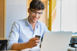 A young man using a cell phone and laptop to compare Arizona SR22 quotes.