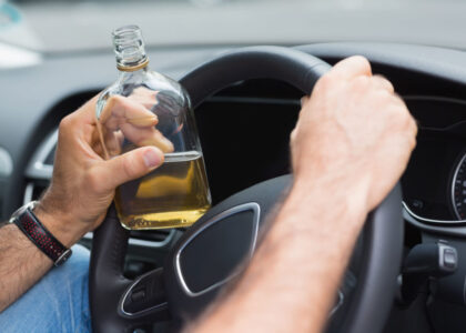 Person holding a bottle of alcohol while driving, illustrating the dangers of DUI and its implications for insurance in Florida.