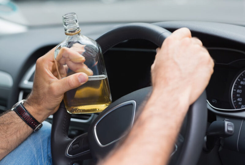 Person holding a bottle of alcohol while driving, illustrating the dangers of DUI and its implications for insurance in Florida.
