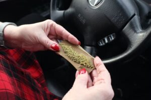 A woman rolling a joint while sitting behind the wheel of a car may need Florida non-owner FR-44 insurance if driving impaired.