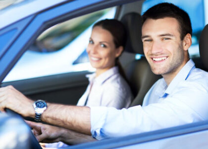 Smiling man and woman inside a car, representing the importance of auto insurance and safe driving for high-risk drivers.