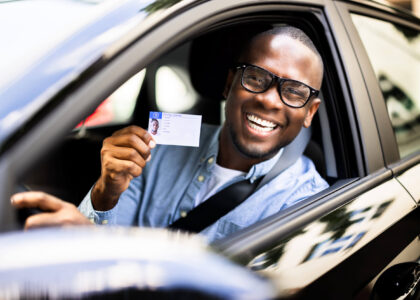 A happy driver behind the wheel of his car showing his reinstated driver's license after filing Colorado SR22 insurance easily.