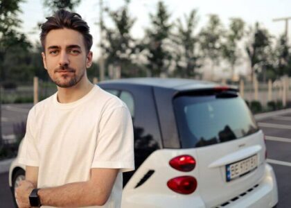 Young man in a white t-shirt standing in front of a small white car after learning how long he will need SR22 insurance in Colorado.
