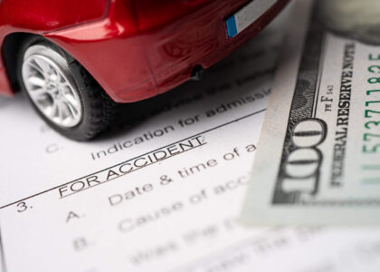 A toy car, an accident report, and a one-hundred dollar bill signifying Colorado SR22 insurance costs.
