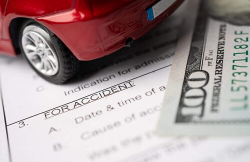 A toy car, an accident report, and a one-hundred dollar bill signifying Colorado SR22 insurance costs.
