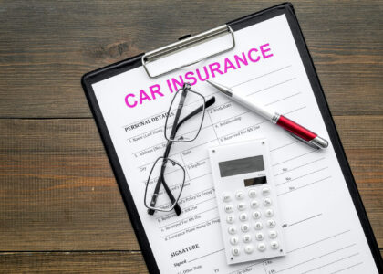 A clipboard with a car insurance quote form, eyeglasses, a pen and calculator, representing calculation of a customer's Alabama SR22 insurance cost.