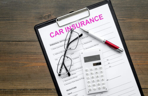 A clipboard with a car insurance quote form, eyeglasses, a pen and calculator, representing calculation of a customer's Alabama SR22 insurance cost.
