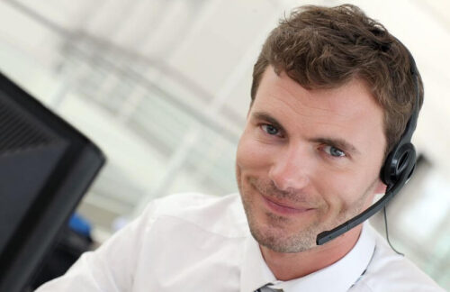 A friendly male car insurance agent at a computer with a phone headset is ready to assist clients to file an SR22 insurance certificate in Kansas.