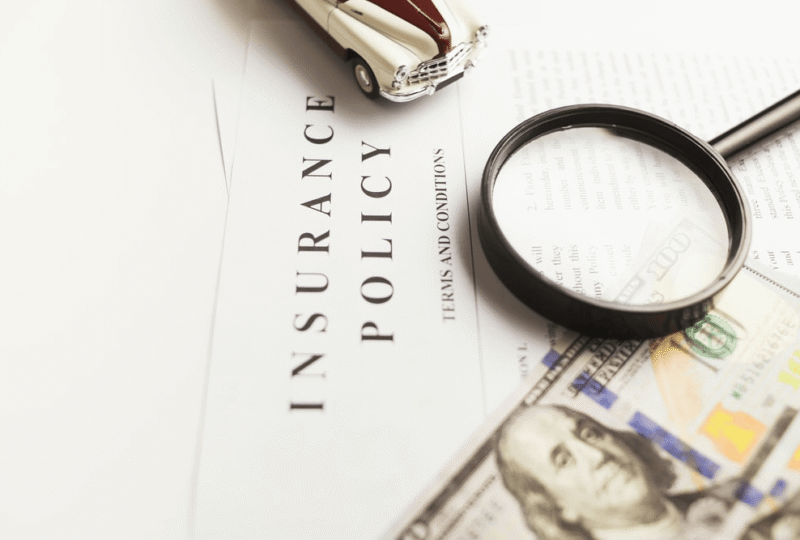 A photo of an insurance policy, cash, a toy car and magnifying glass represent obtaining an Oregon SR22 insurance policy to reinstate your license.
