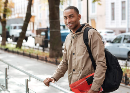 A young man pausing at a sidewalk railing carrying a backpack and red folder, reflecting on how long he will need to keep SR22 insurance in Tennessee.