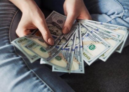 A person's hands fanning out a number of $100 bills represents the possible additional cost of SR22 insurance in Tennessee.