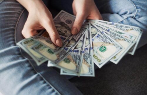 A person's hands fanning out a number of $100 bills represents the possible additional cost of SR22 insurance in Tennessee.