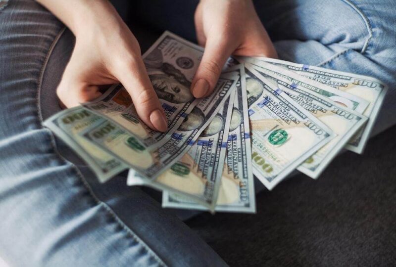 A person's hands fanning out a number of $100 bills represents the possible additional cost of SR22 insurance in Tennessee.
